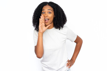 Fototapeta na wymiar Excited African American woman shouting. Portrait of happy young female model with dark curly hair in white T-shirt looking at camera with hand near open mouth, calling someone. Advertisement concept