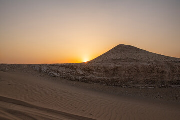 Fototapeta na wymiar Sun is rising in the desert . Sunrise-sunset desert landscape photo. Gulf desert sunrise with sand dunes and sand pattern visible with sun shine.
