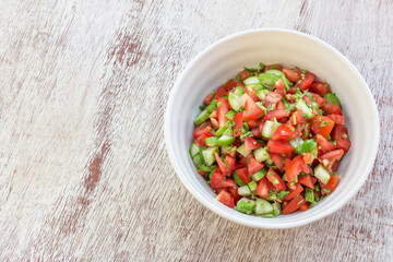 Healthy food tomato cucumber salad in bowl on white wood background.