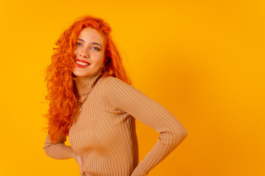 Red-haired woman on a yellow background, studio shot, looking up and smiling, copy space