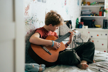 Romantic teenage redhead girl learning to play the guitar while sitting in the room.