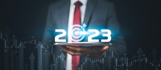 Businessman holds tablets with target and number new year 2023 on the business graph background,...