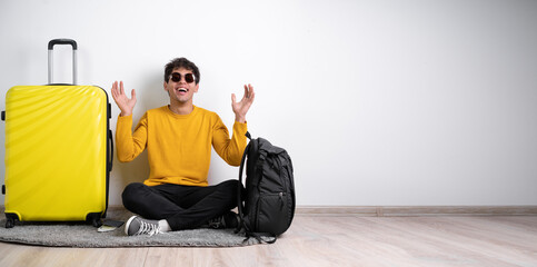 Full height traveler tourist man in sweater with suitcase sit, happy expression and raising arms isolated on white background Passenger travel abroad weekends getaway. Air flight journey
