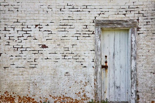 Abandoned white brick building with old decaying wood door and lichen