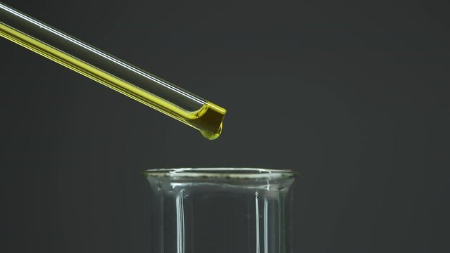 Oil drips from pipette into bottle. Obtaining oil extracts. Medical bottle on dark background. The extract flows through the glass tube. Yellow liquid. Oil industry. Oil purification from impurities