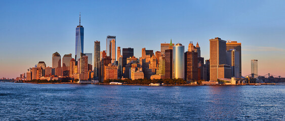 Panoramic golden hour skyline of southern Manhattan New York City skyline from ferry with water in...