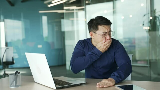 Sick asian businessman IT programmer with glasses suffering from stomach ache feeling bad nausea at modern workplace Unhealthy employee holding belly with poisoning and vomiting reflex at desk indoor 
