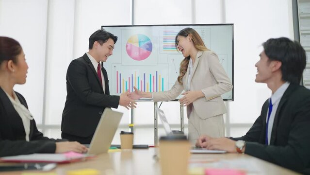 Two business professionals, Asian man and women make presentations and shake hands to congratulate on success of work in meeting room at office