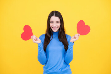 Happy woman hold red heart. Beautiful female model posing on isolated yellow background. Cheerful positive cute pretty tender girl with heart.