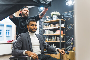 Barbershop concept. Male Indian client sitting on a hairdresser chair and looking at camera while...
