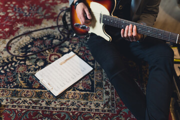 Guitarist sitting on patterned carpet with electric guitar and note sheet. Top view. Unrecognizable...