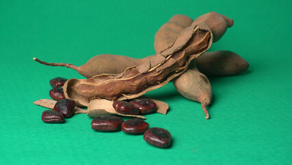 Ripe tamarind fruit, leaves and some tamarind seeds isolated on green background.