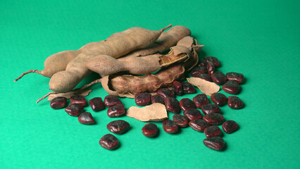 Ripe tamarind fruit, leaves and some tamarind seeds isolated on green background.
