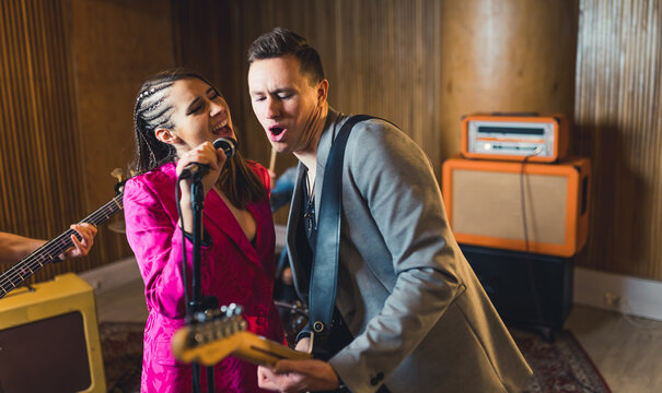 Vocalist and guitarist. Indoor portrait of caucasian woman singer singing to the microphone with male guitarist during a concert. High quality photo