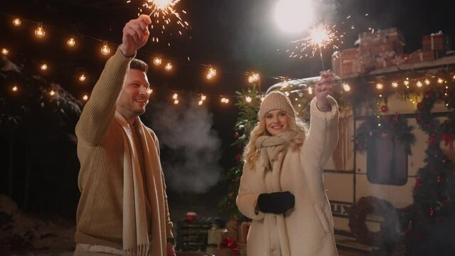 happy married couple in merry Christmas party in nature in cold night, burn sparklers and smile