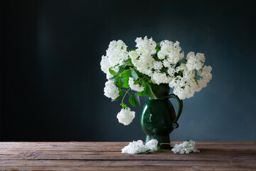 white hydragea in vintage jug on wooden table on background dark wall