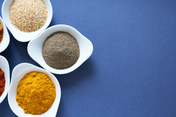 Dried garlic, black pepper and turmeric in small containers on a blue background. 