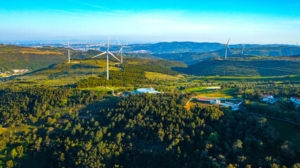Wind farm generating green energy. Wind turbines with blades in field aerial view. Alternative energy. Scenic Aerial view of wind turbines farm over green beautiful landscape.