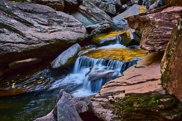 Up close to small cascading waterfall surrounded by lichen and boulders in soft light