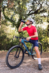 Obraz premium young cyclist drinking water while resting during his mountain bike training ride, concept of freedom and sport in nature