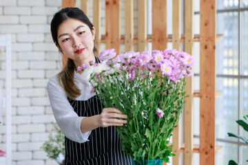 Millennial Asian young female flower shopkeeper decorator florist employee worker in apron standing smiling taking care fresh flowers bunch bouquet in floral store.