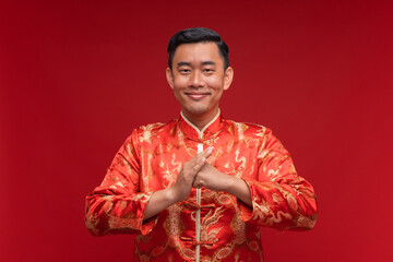 Young asian man wearing Chinese red shirt make a wish on red background for Chinese new year...
