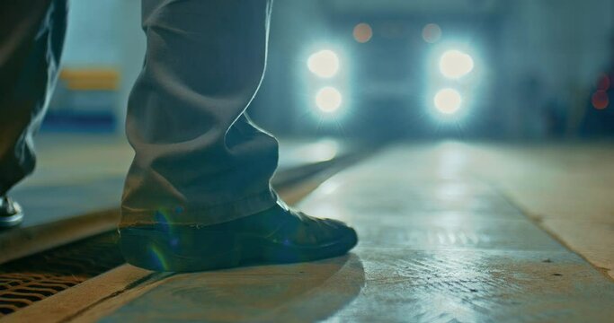 Car is approaching an auto mechanic at a service station. Legs of an auto mechanic close-up. The car pulls into a car service or garage.