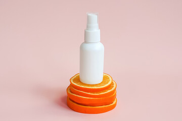White cosmetic spray bottle and orange slices podium on pink background. Hair natural oil, body...
