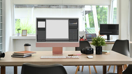 Creative office studio interior, photo editor workstation with blank screen computer, camera and supplies on wooden table