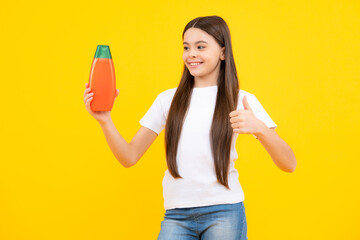 Teenager child girl showing bottle shampoo conditioners or shower gel. Hair cosmetic product. Bottle for advertising mock up copy space. Happy teenager portrait. Smiling girl.