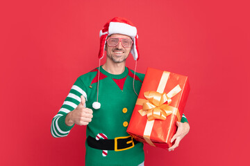merry christmas gift. thumb up. cheerful elf man in earflap santa claus hat.