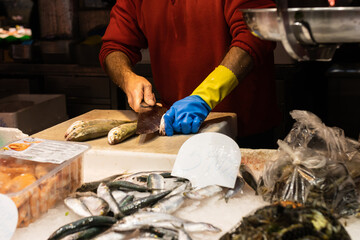 Unrecognizable fish vendor filleting a fish in a market, selective focus on the blue and yellow glove.