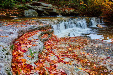 Fall leaves cover layers of rocks by small waterfall in river