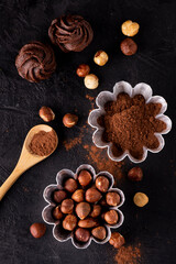 view from above. Aluminum molds for cakes with hazelnuts and cocoa powder and some chocolate kisses on a textured dark background.
