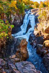 Obraz premium Rocky cliff gorge canyon with large heavy waterfalls and fall forest