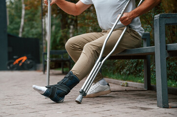 Close up view of the legs. Man with crutches is in the park outdoors