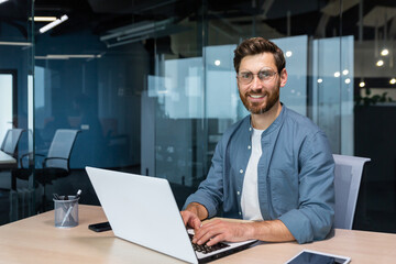 Portrait of mature businessman inside modern office, senior man in shirt smiling and looking at...