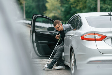 Injured man with crutches is going out from the car