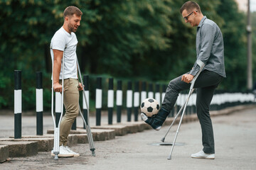 Obraz premium Having fun, playing soccer. Two men with crutches is outdoors on the road