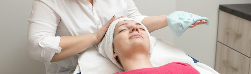 Fototapeta na wymiar Face skin care. Beautician applying beauty oil mask on face using brush In spa salon