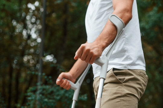 Close up view. Man with crutches is in the park outdoors. Having leg injury