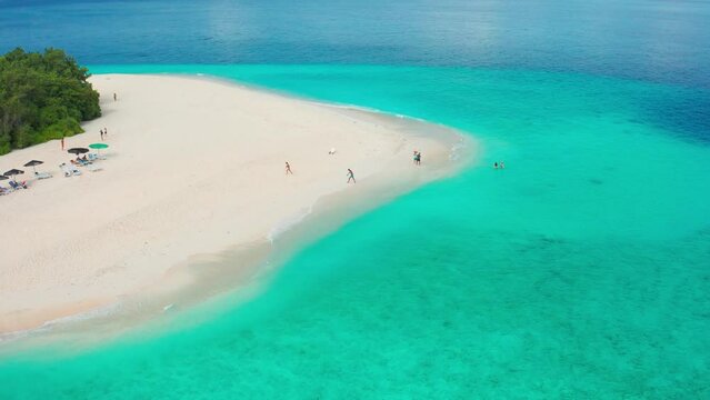 Tourists on a white sandy beach with turquoise sea on local island Ukulhas in the Maldives. Aerial drone view.