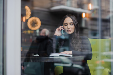 A beautiful young woman in a black dress sits in a cafe by the window and drinks coffee. Coffee break