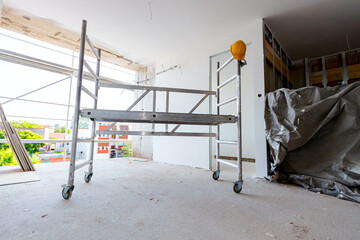 Moveable scaffold with wheels in the building under construction, yellow hardhat is on it - obrazy, fototapety, plakaty