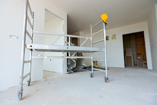 Moveable scaffold with wheels in the building under construction, yellow hardhat is on it