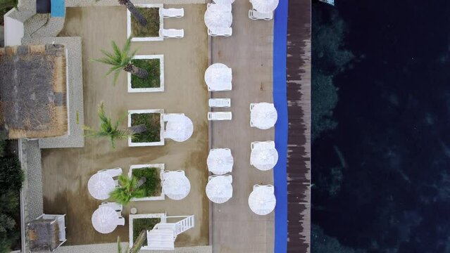Bird aerial drone top view morning empty resort, white sun beds, chairs, loungers, umbrellas under palm tree, sea view with horizon, calmness and relaxation, Inspirational beach resort hotel vacation