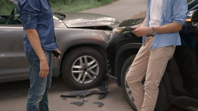 Two drivers at side of the road exchanging car insurance details after traffic accident using mobile phones. Close up of handshake of drivers after an accident.