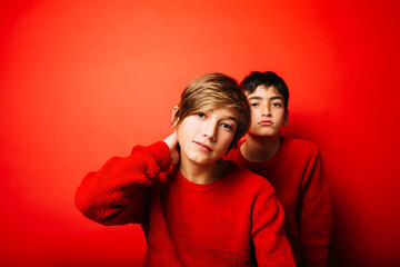 Obraz premium Studio portrait of two pre-adolescent boys, wearing a red sweater, playing over a red background