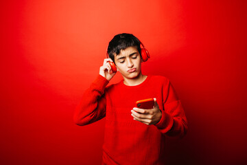 Studio portrait of a pre-adolescent boy, wearing a red sweater and red headphones over a red background, listening music and dancing