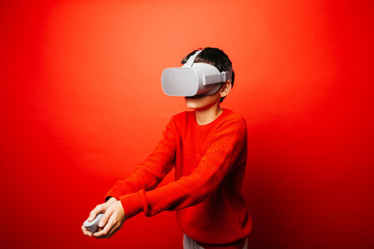 Studio portrait of a pre-adolescent boy with virtual reality glasses over a red background